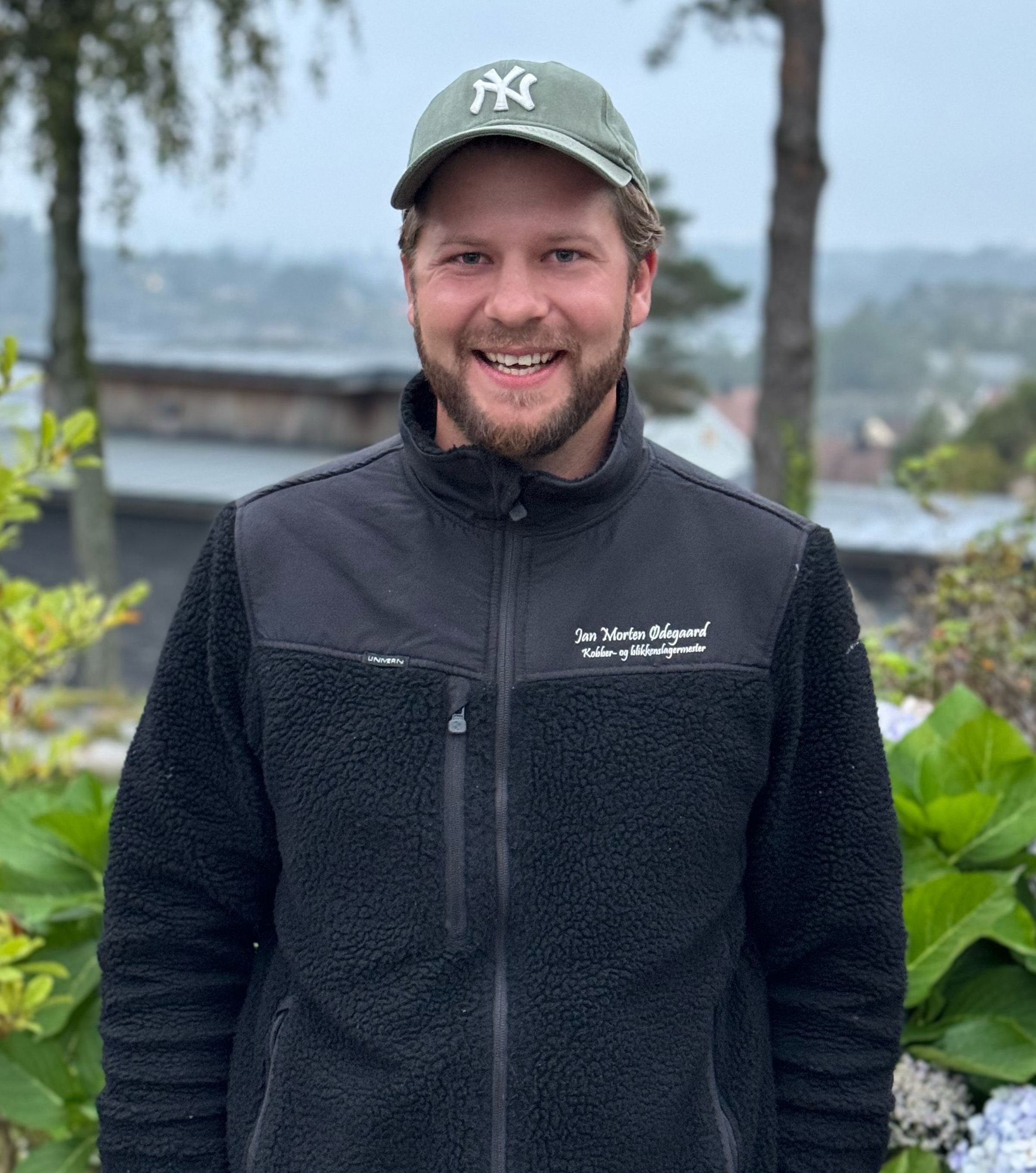 Smilende mann med svar jakke og grønn caps